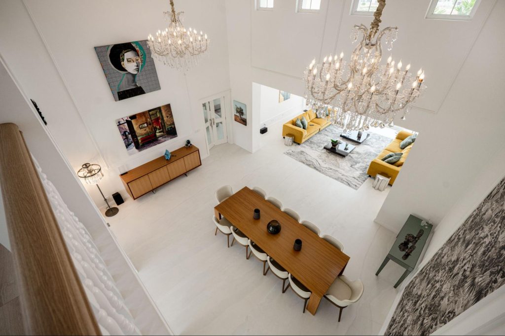 Elegant double-height living and dining space design by Smart Renovation for Villa Jasmine featuring crystal chandeliers and modern art pieces.
